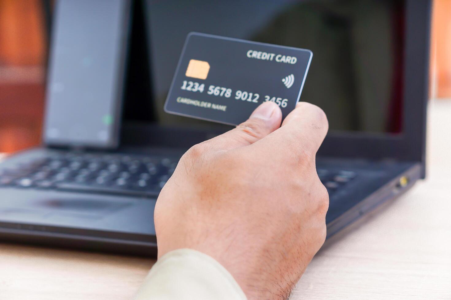 A person holds a credit card in front of a laptop, indicating online transactions. photo