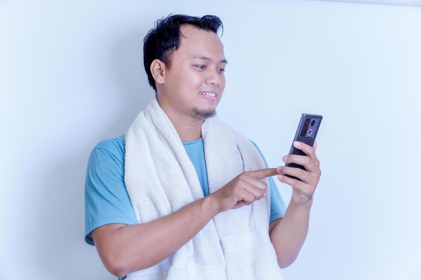 A man in a towel smiles while using his smartphone, enjoying a relaxed moment. photo