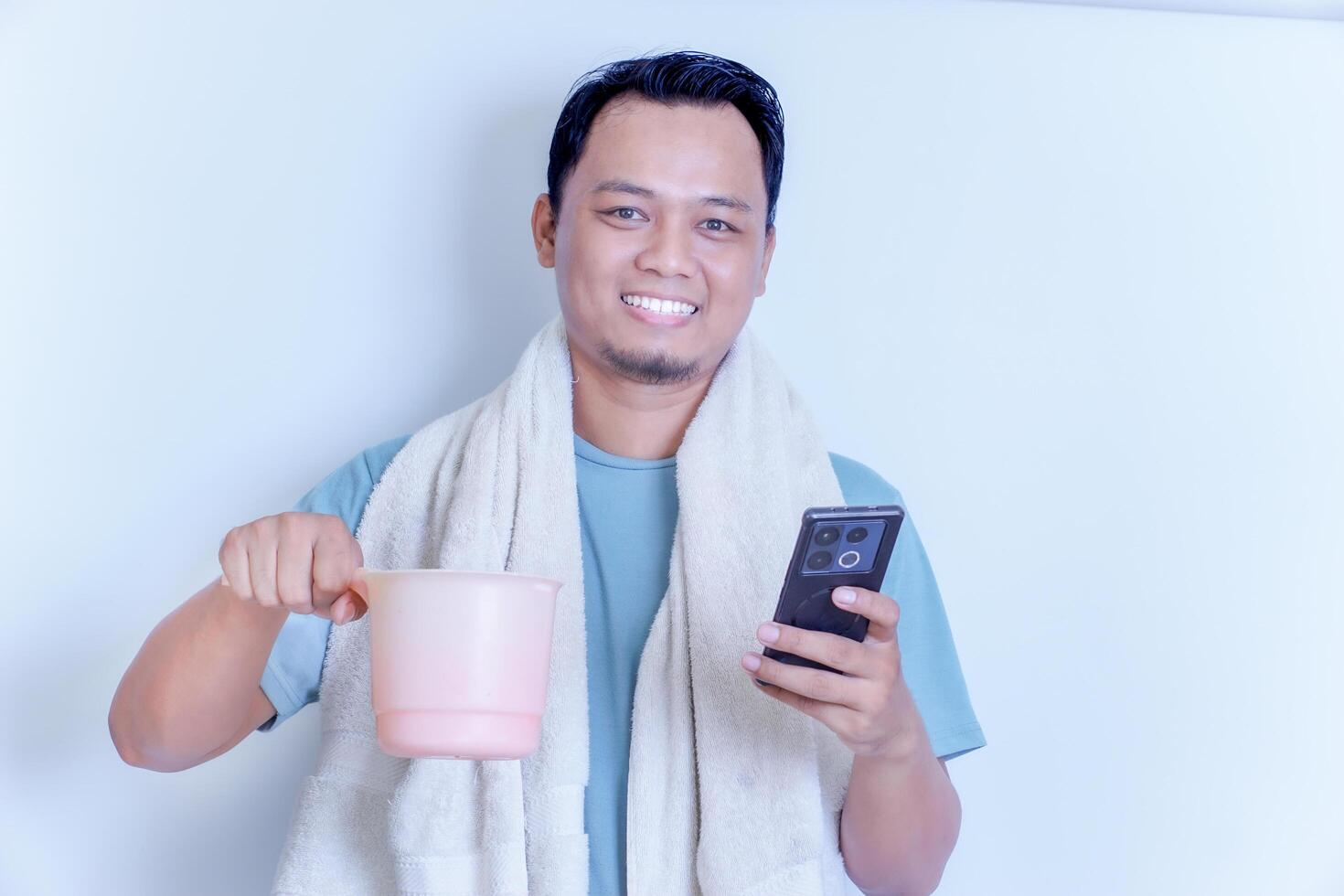 a smiling Asian man with a towel over his shoulder while holding his smartphone and a dipper photo