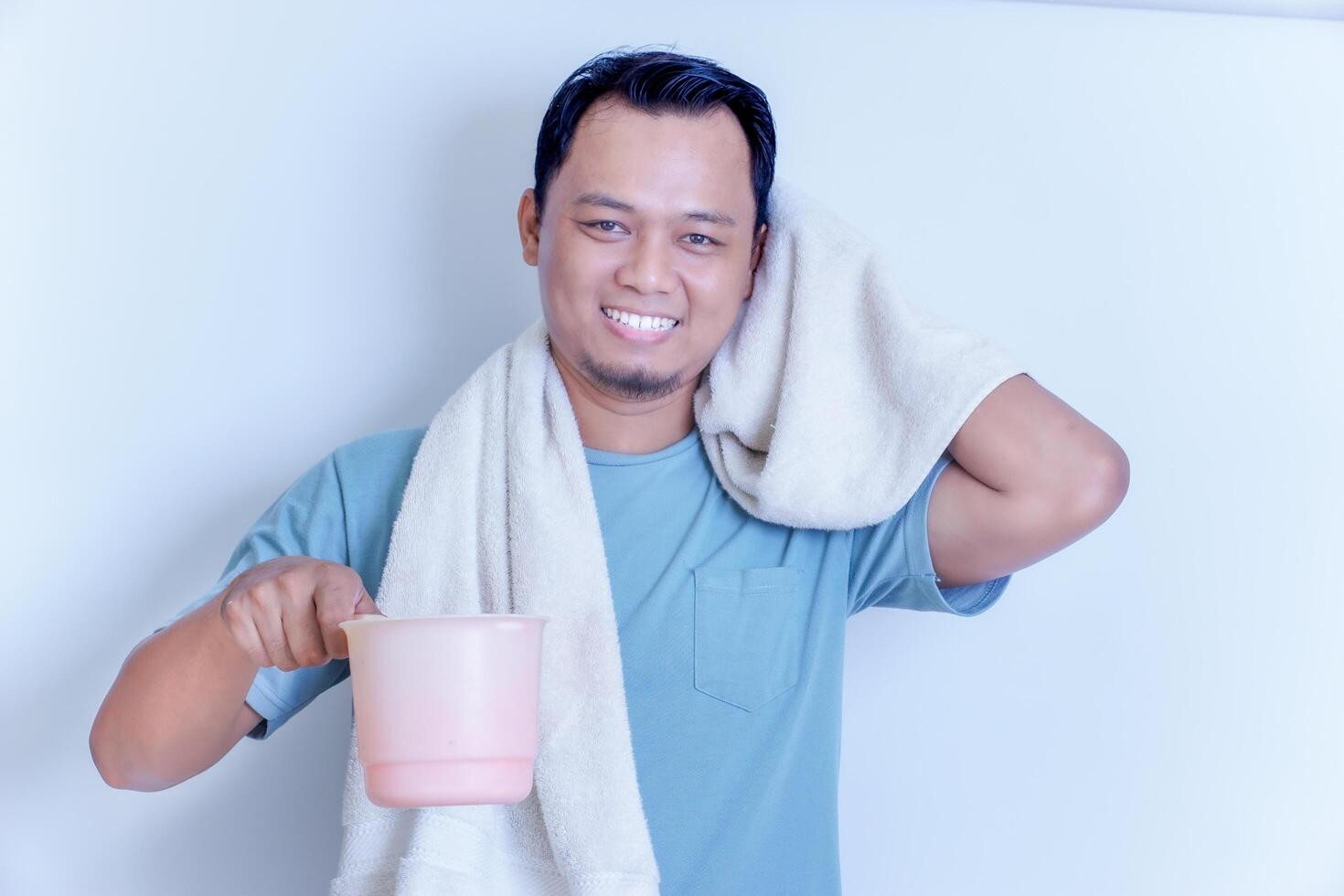 An Asian man smiled while holding a pink dipper and a towel draped over his shoulder. photo
