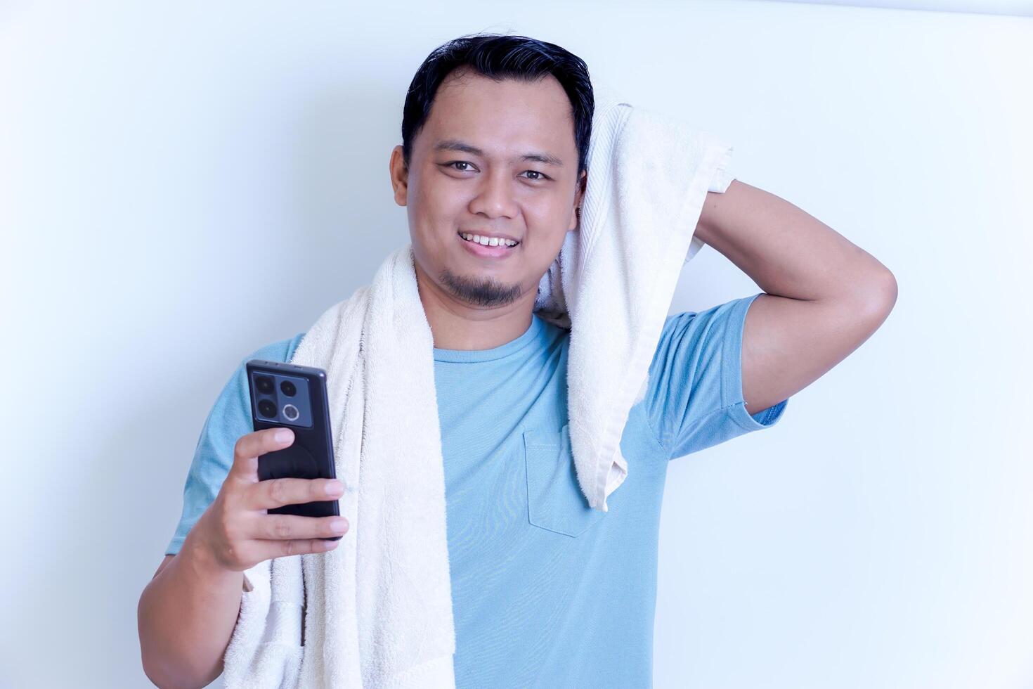 A Asian man is smiling while looking at his phone, holding a towel over his shoulder. photo