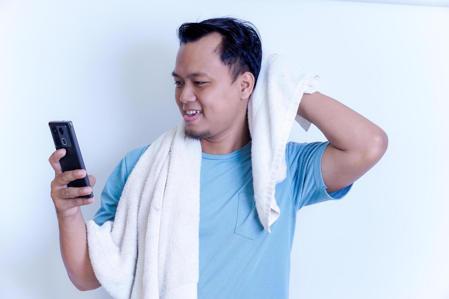 A Asian man is smiling while looking at his phone, holding a towel over his shoulder. photo
