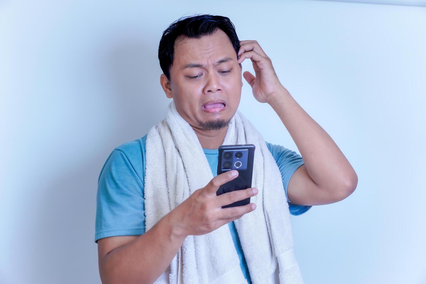 Frustrated man checking his phone, deep in thought, with a towel around his neck photo