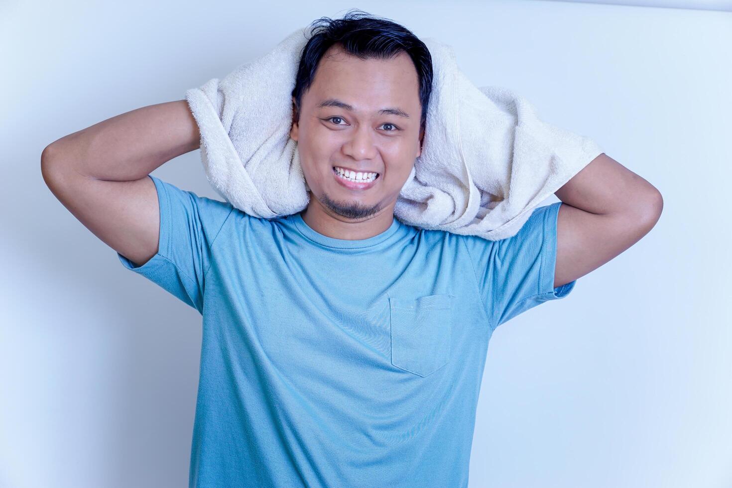 A young Asian man smiling confidently after shower , holding a towel over his shoulder in a bright setting. photo