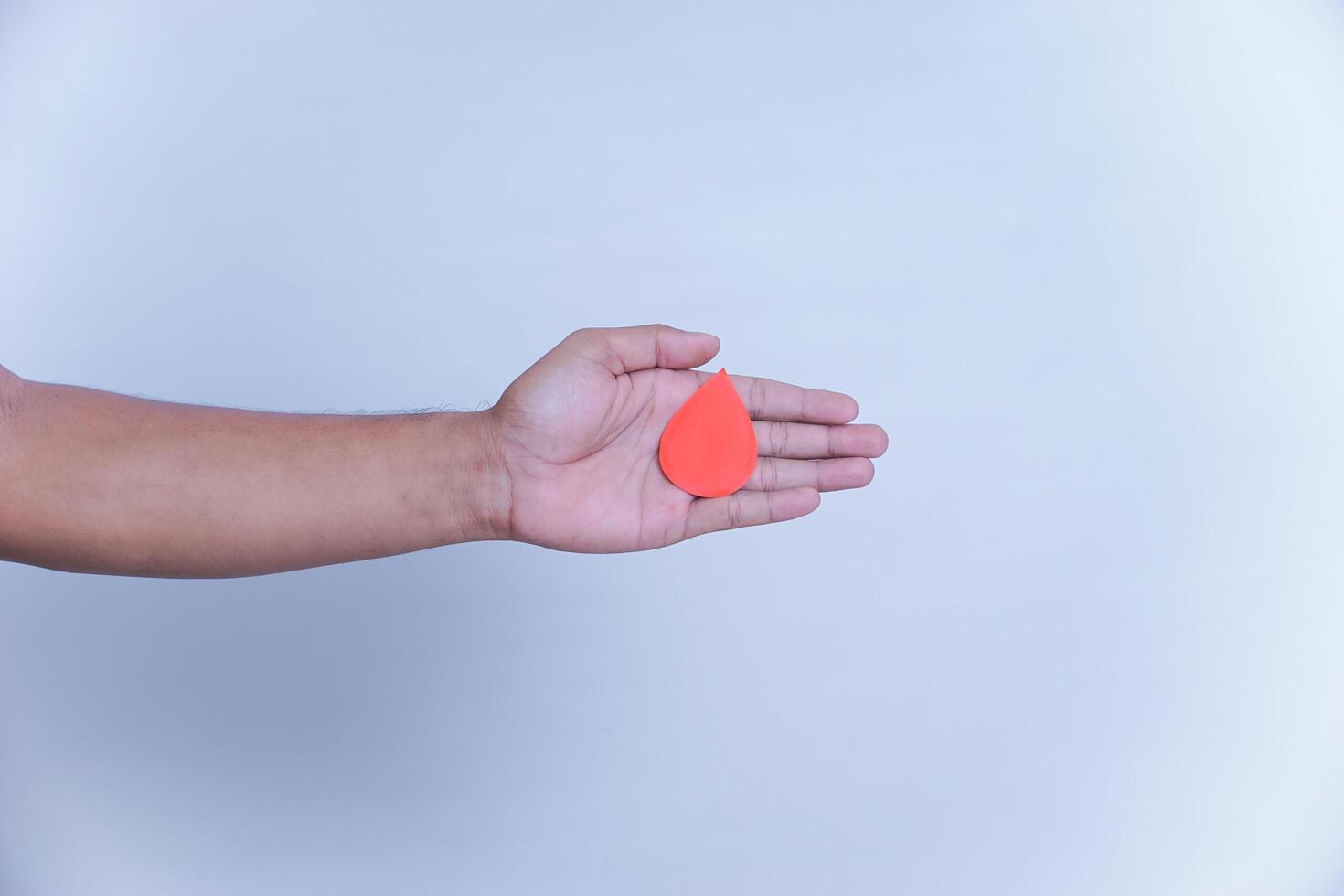 a hand hold a drop of donor blood with white background. world blood donor day concept, photo