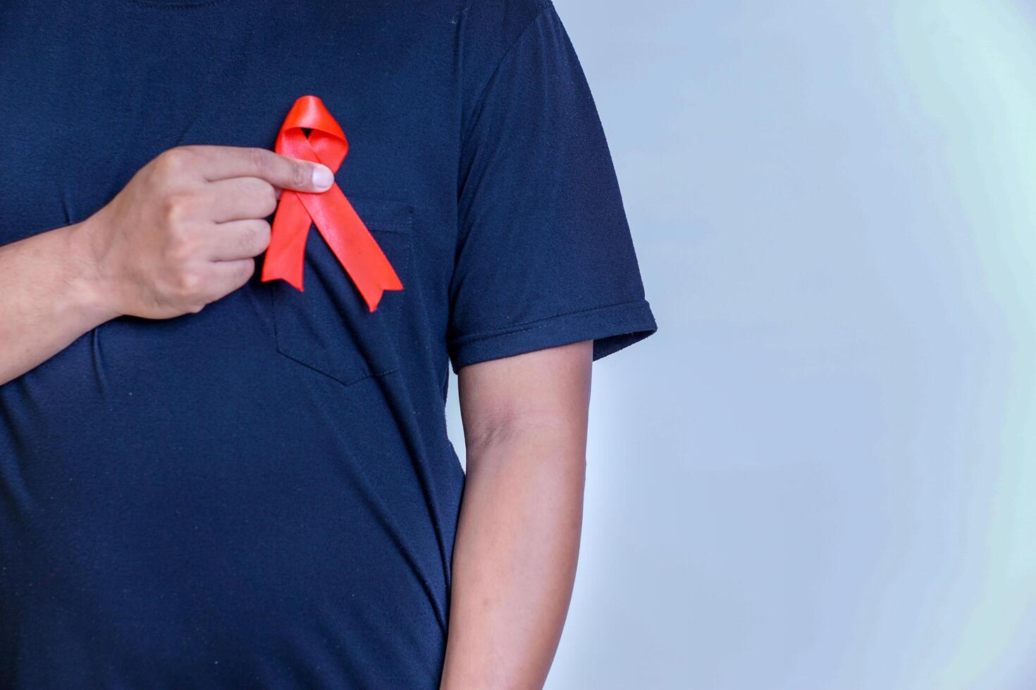 a man holds a red ribbon and tapes it to his chest, symbolizing awareness and support for important causes photo