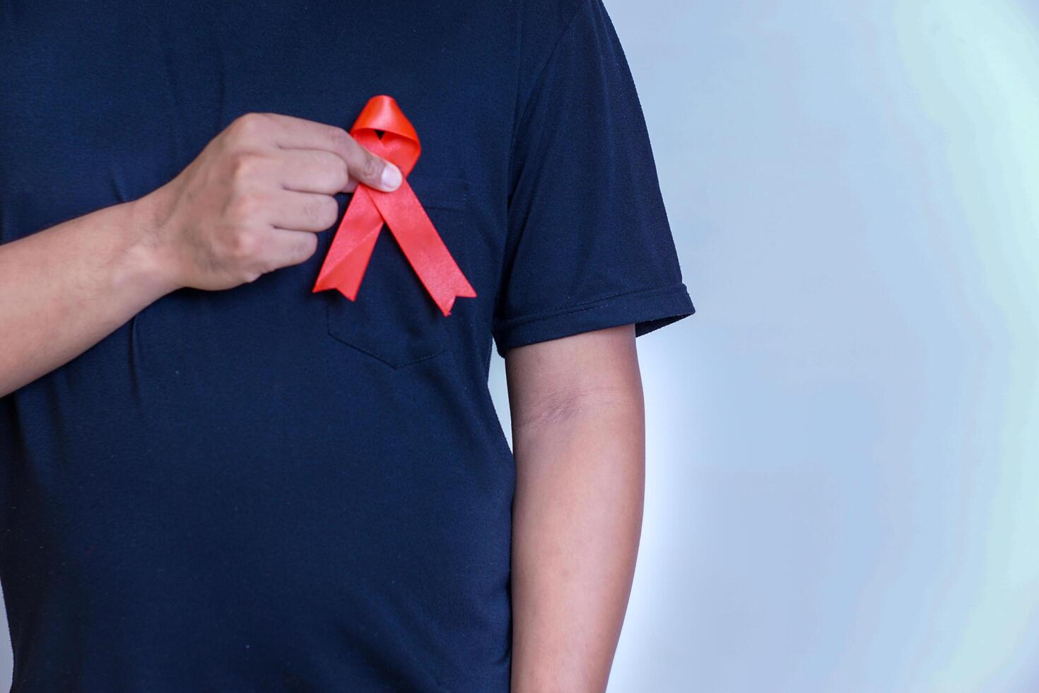 a man holds a red ribbon and tapes it to his chest, symbolizing awareness and support for important causes photo