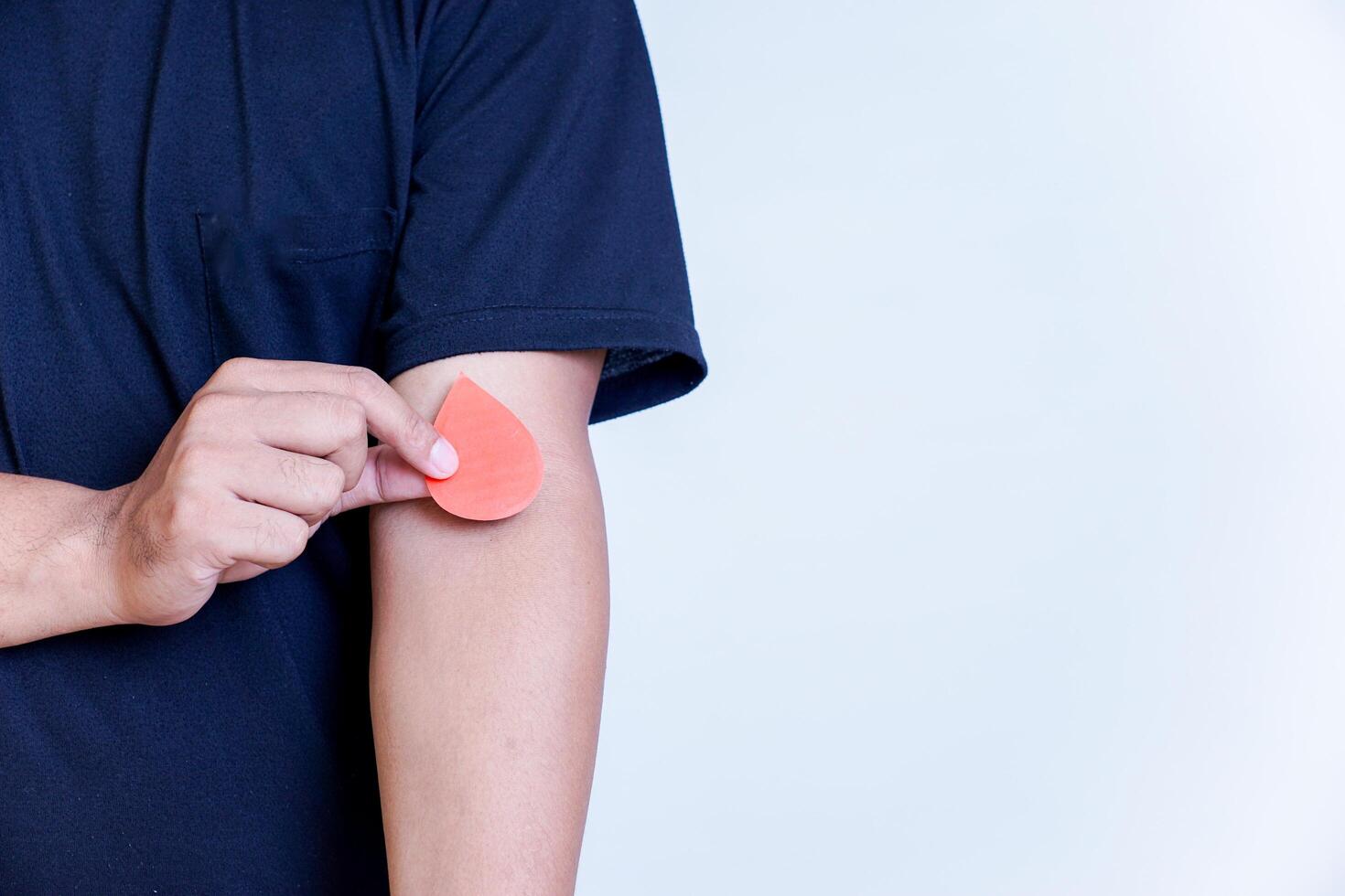 A person holds a red paper drop shape on their arm, symbolizing blood donation awareness. photo