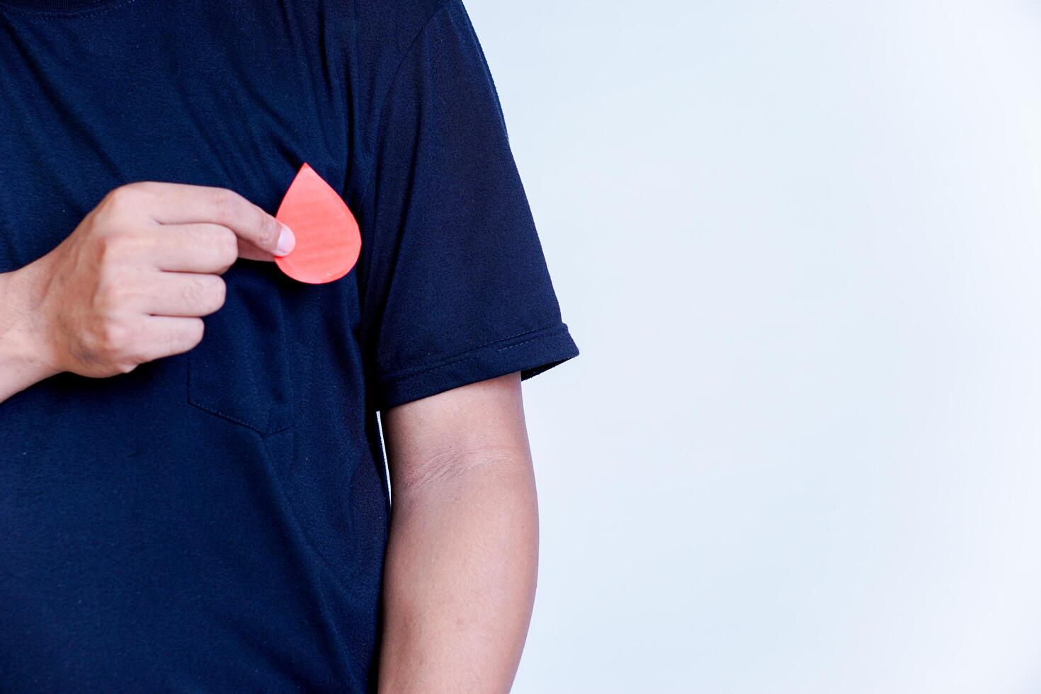 a man's hand holds a drop of donor blood close to his chest on a white background. concept of world blood donor day, photo