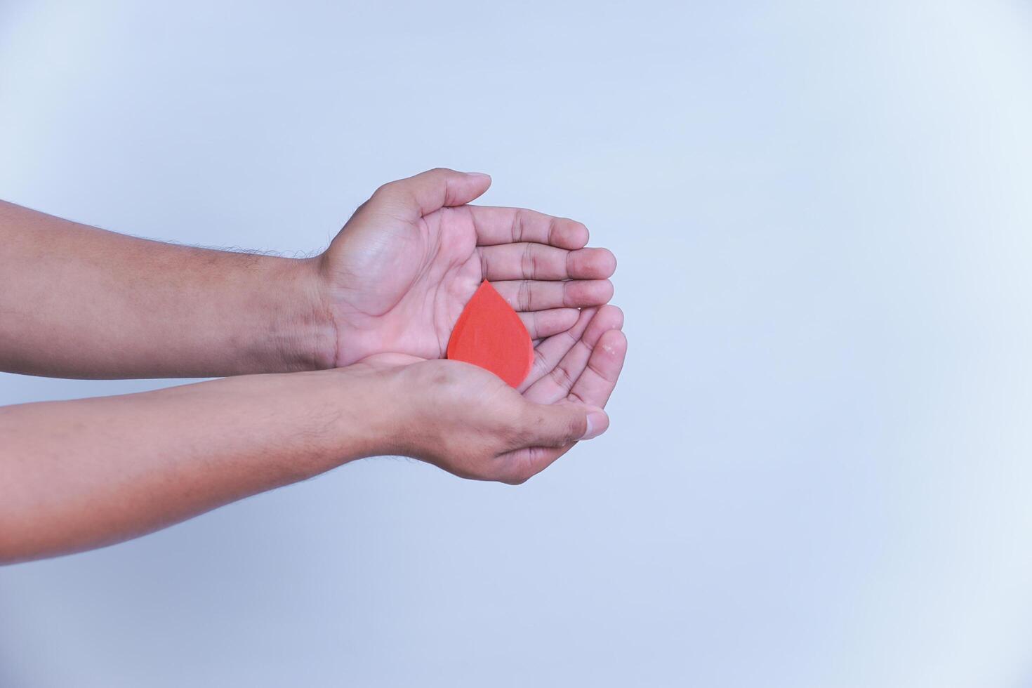 a hand hold a drop of donor blood with white background. world blood donor day concept, photo