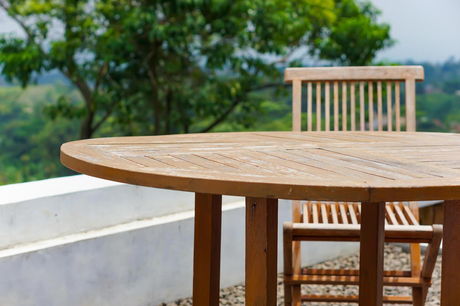 A wooden dining table and chair set in a serene outdoor setting with green foliage. photo