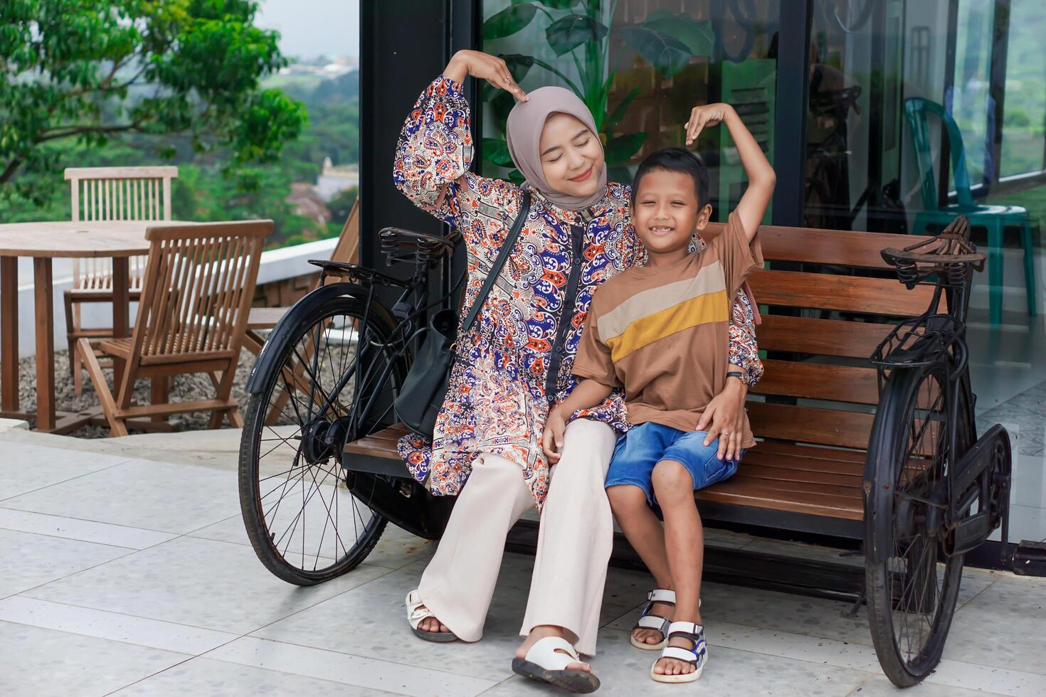 A asian mother wearing hijab and son share a joyful moment sitting on a bench. concept of mother's day photo