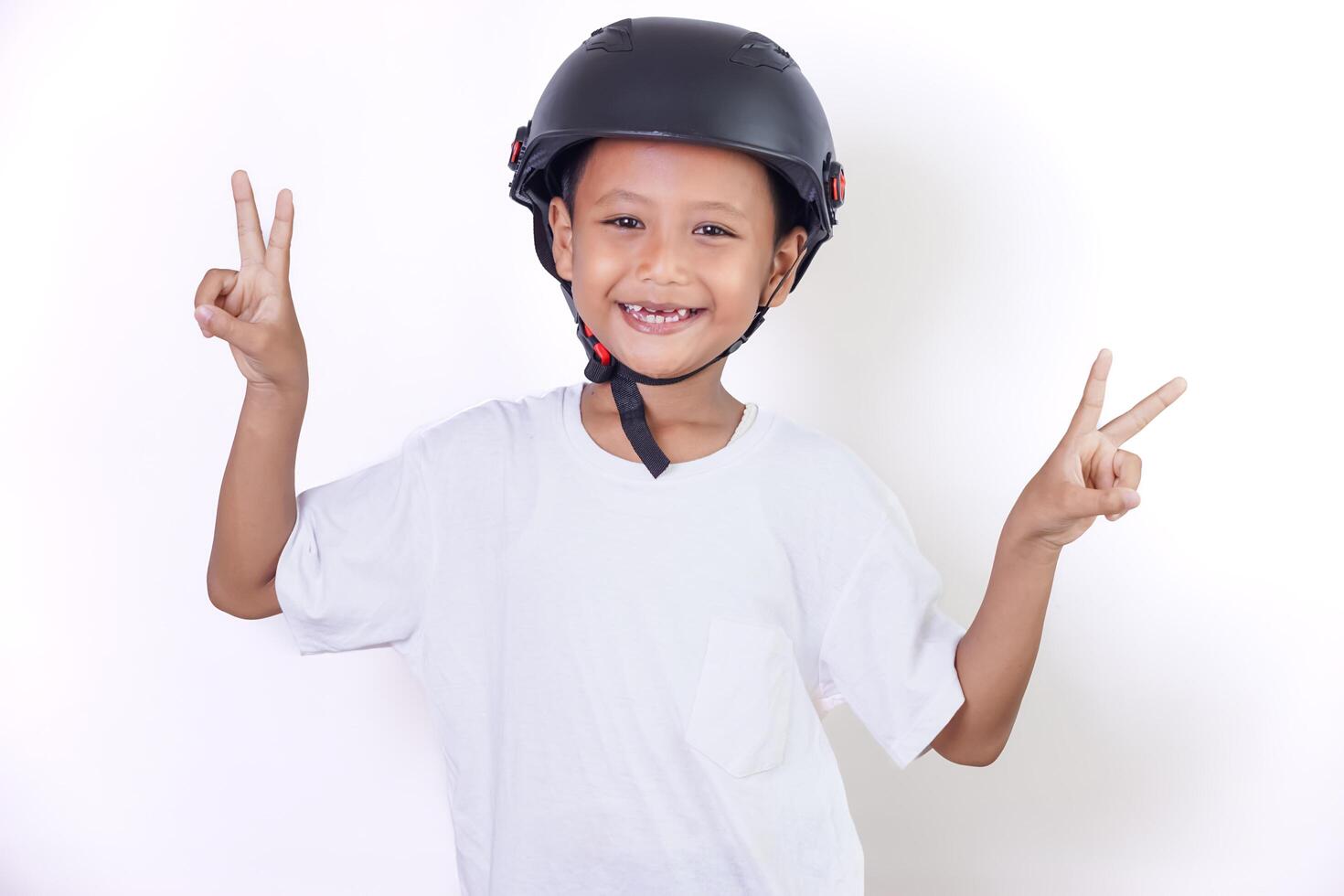 A cheerful asian child wearing a helmet, showing a peace sign with both hands. photo