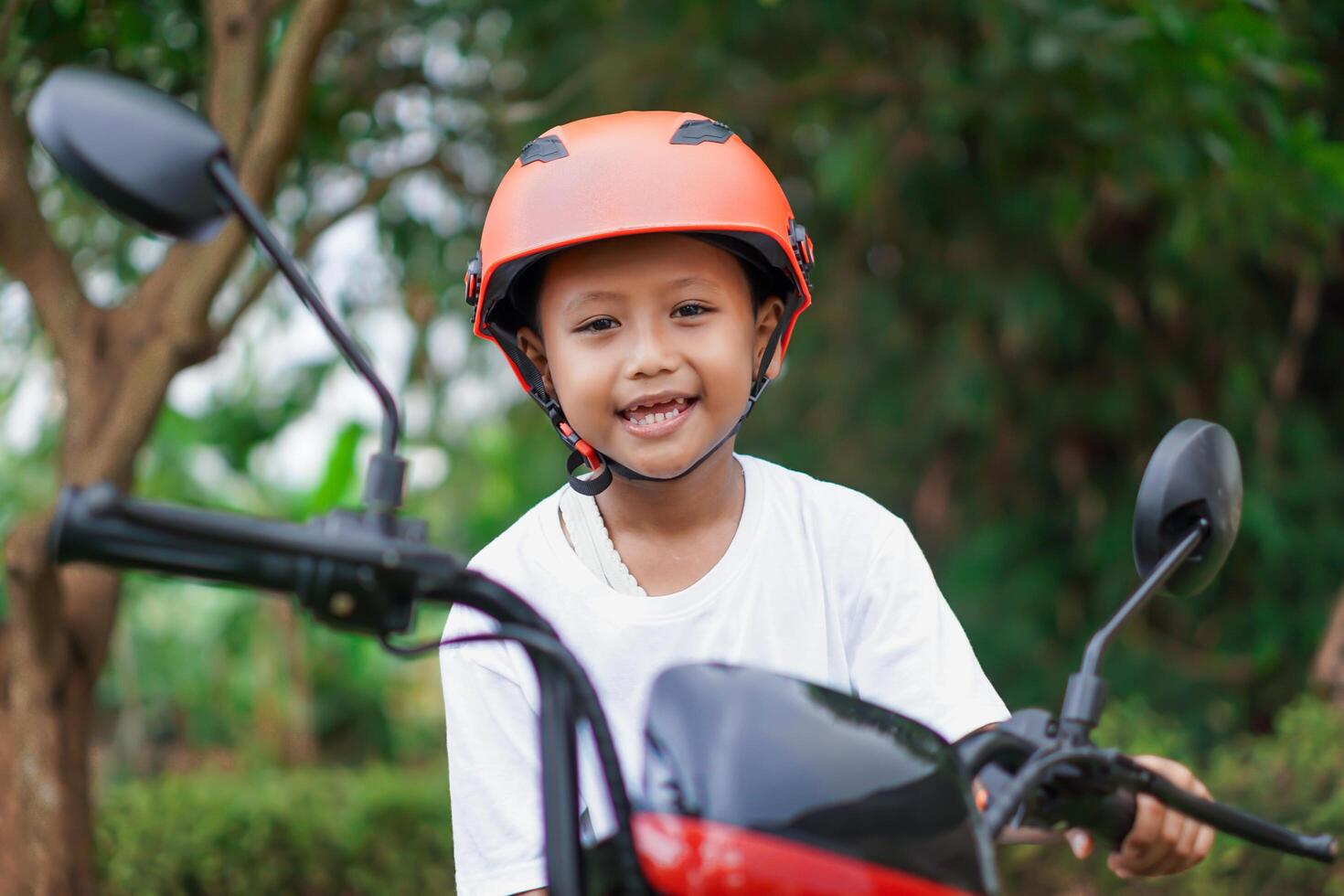 A happy asian boy in a bright helmet poses confidently on a electric scooter photo