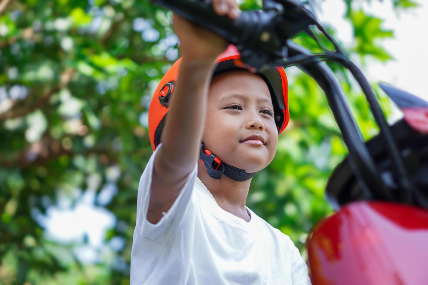 A joyful asian boy enjoying a ride on his red electric scooter, wearing a bright orange helmet. photo