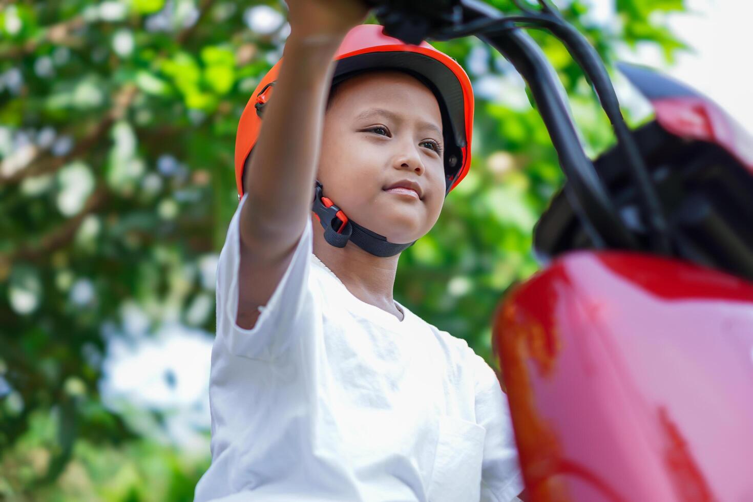 A joyful asian boy enjoying a ride on his red electric scooter, wearing a bright orange helmet. photo