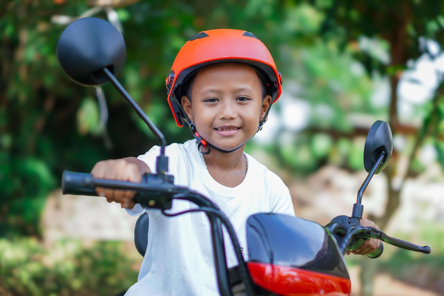 A happy asian boy in a bright helmet poses confidently on a electric scooter photo