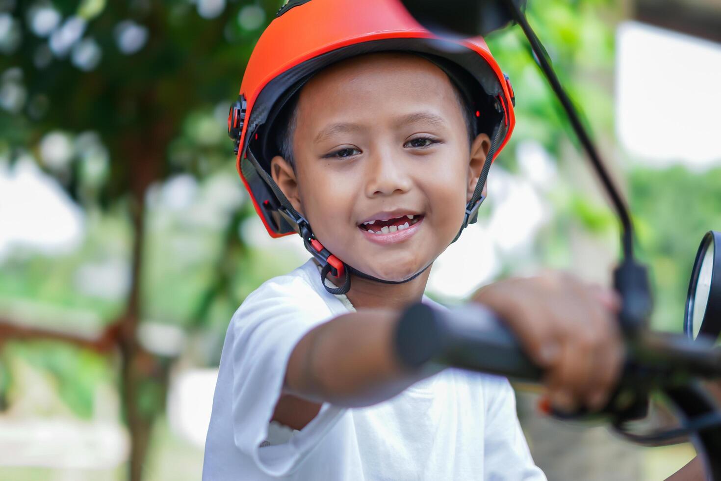 A happy asian boy in a bright helmet poses confidently on a electric scooter photo