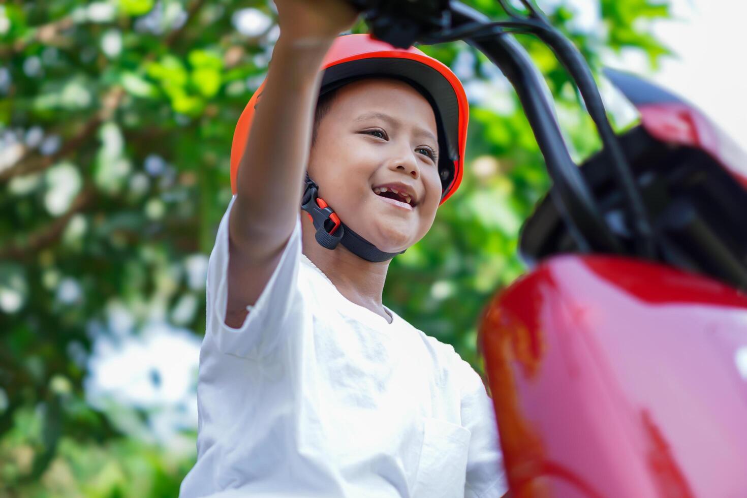 A joyful asian boy enjoying a ride on his red electric scooter, wearing a bright orange helmet. photo