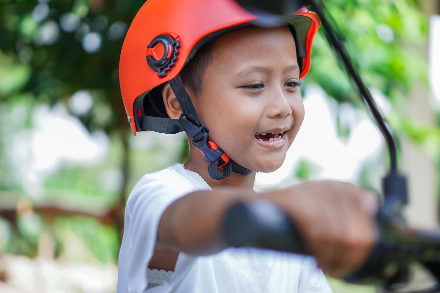 A happy asian boy in a bright helmet poses confidently on a electric scooter photo