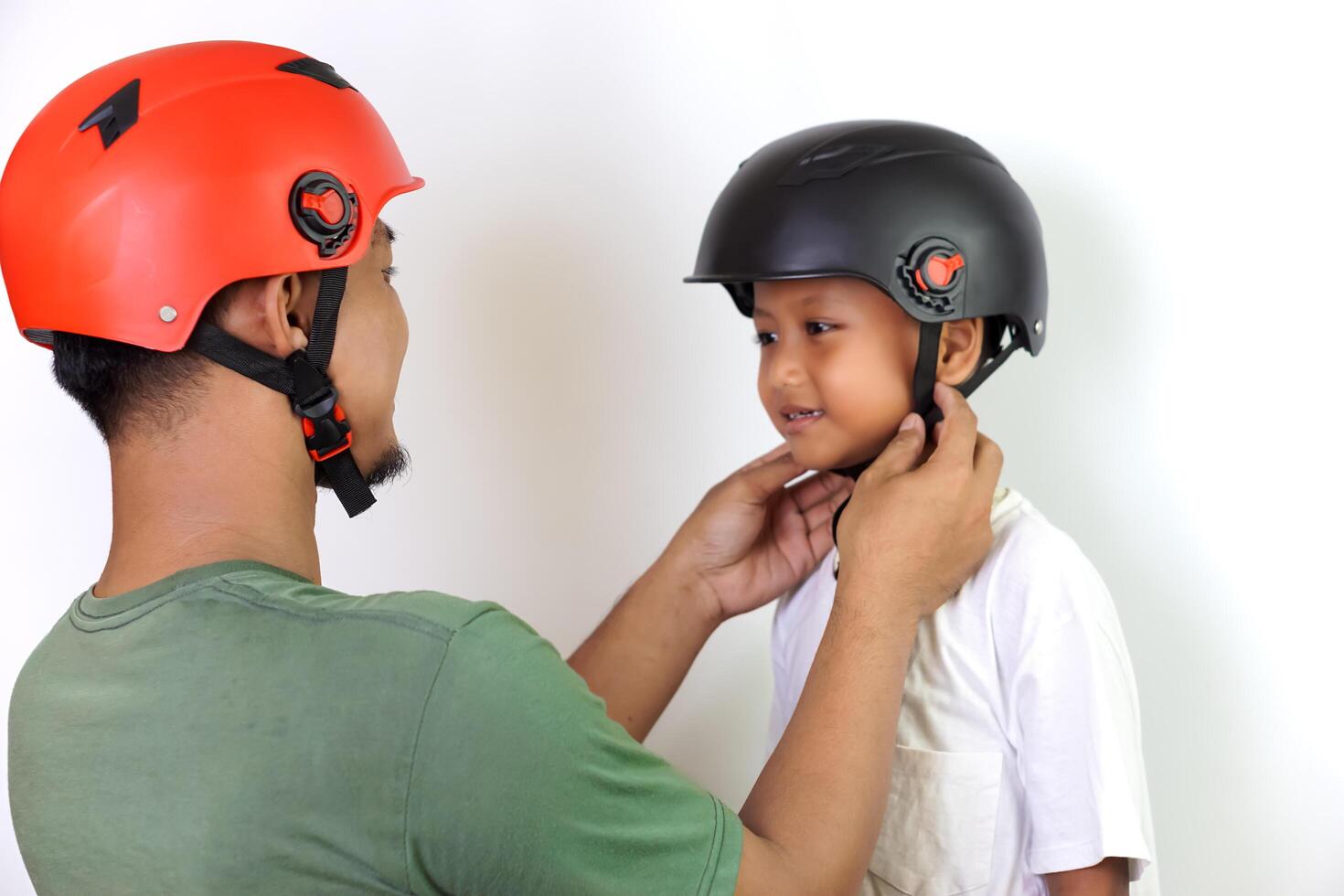A asian father helps his son wear a helmet, ensuring safe and fun outdoor riding. photo