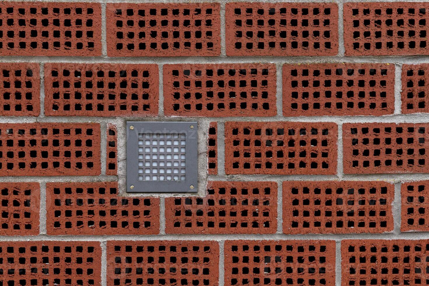 A textured brick wall features hollow red bricks arranged in a pattern photo