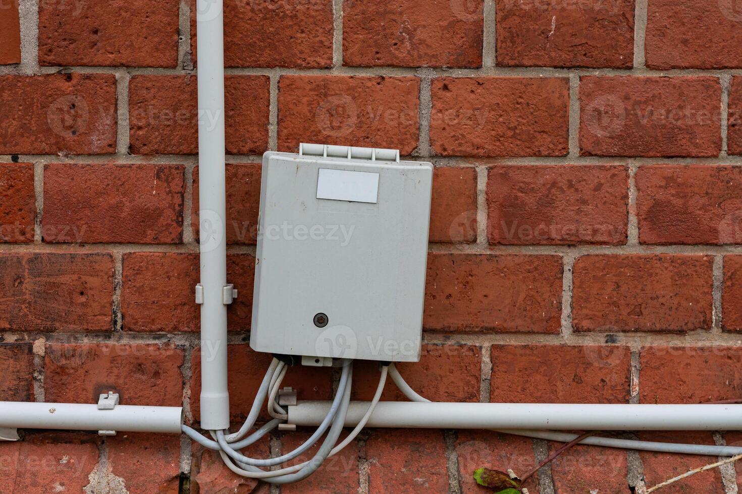 A utility box is securely fastened to a red brick wall, with white photo