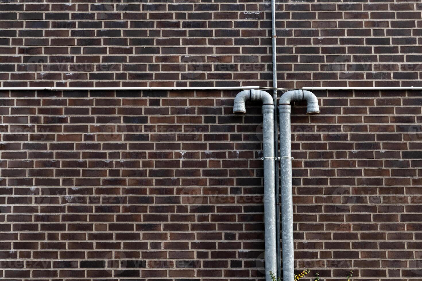 Two metal pipes extend vertically from a brick wall, showcasing a photo