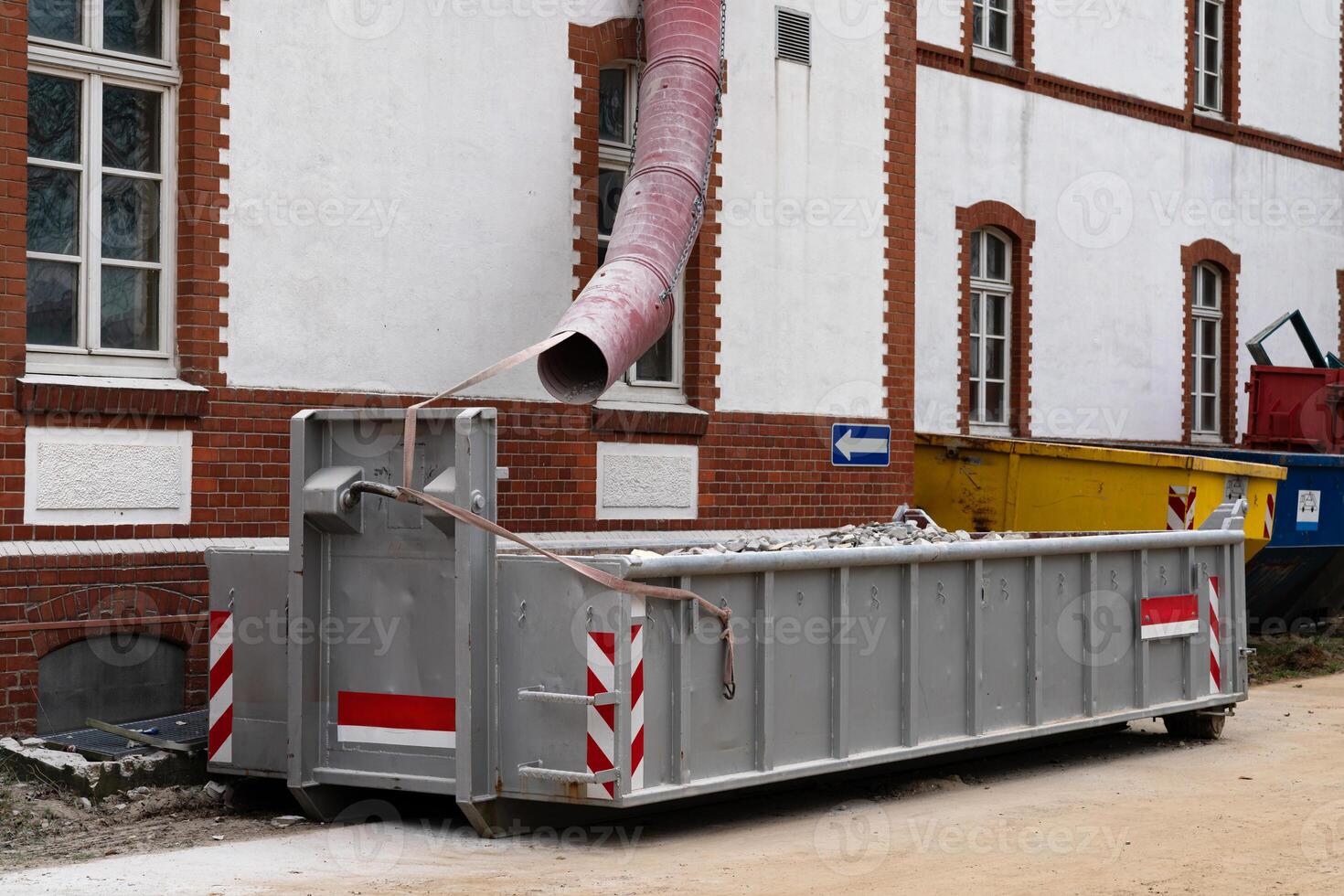 A large waste disposal container sits at a construction site next to a photo