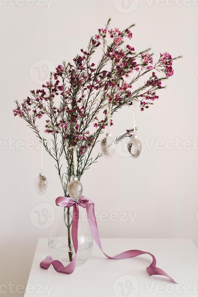 Easter eggs hang on a sprig of flowers in a transparent vase. photo