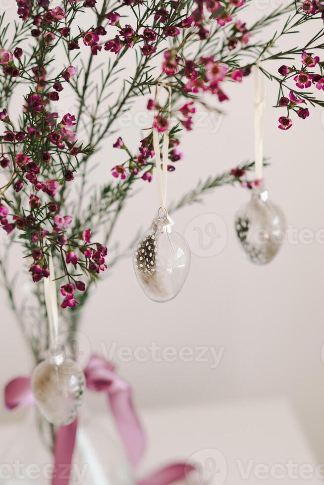 Easter eggs hang on a sprig of flowers in a transparent vase. photo