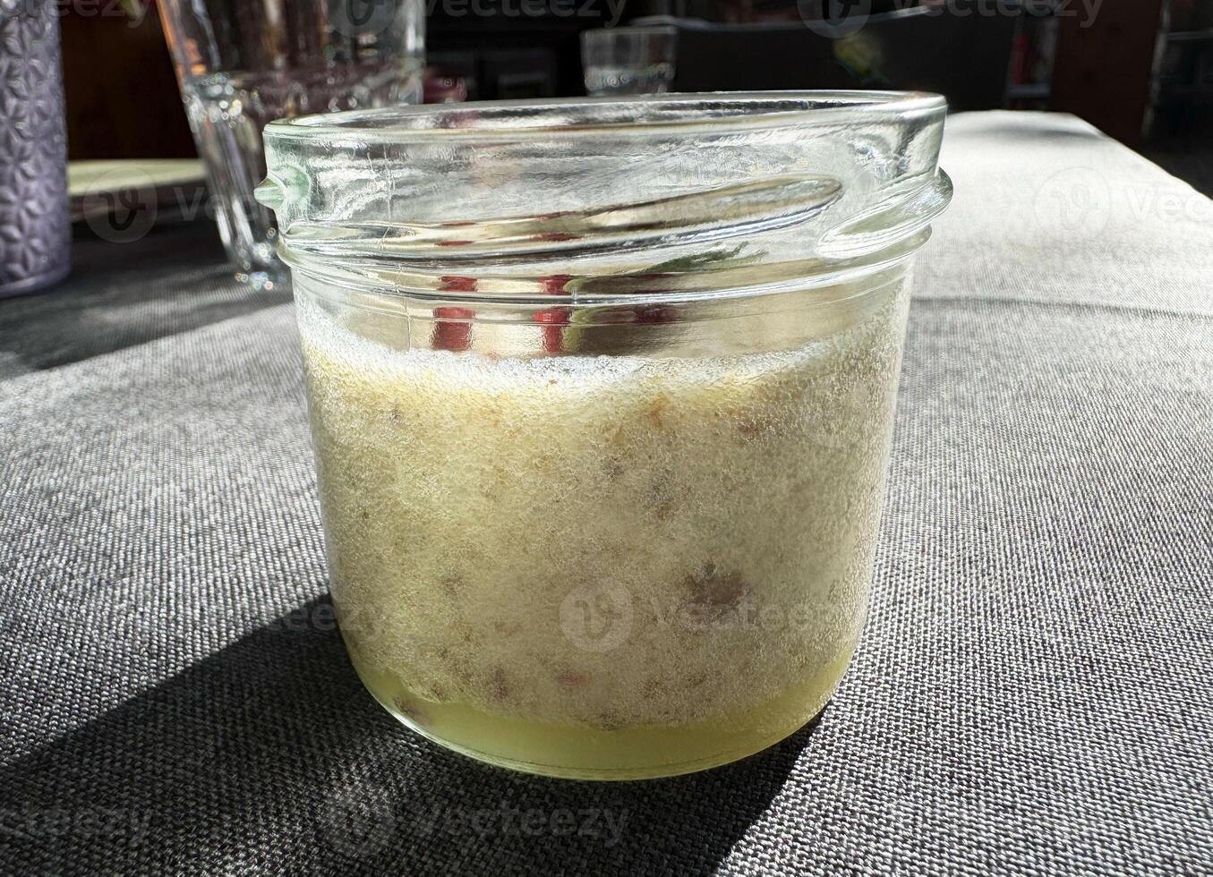 Fermented sourdough starter jar on textured gray fabric in sunlight photo