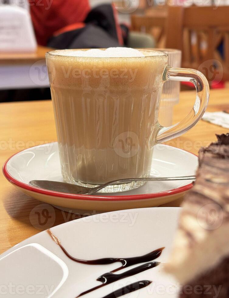 Creamy cappuccino in glass mug on cafe table with chocolate cake slice photo