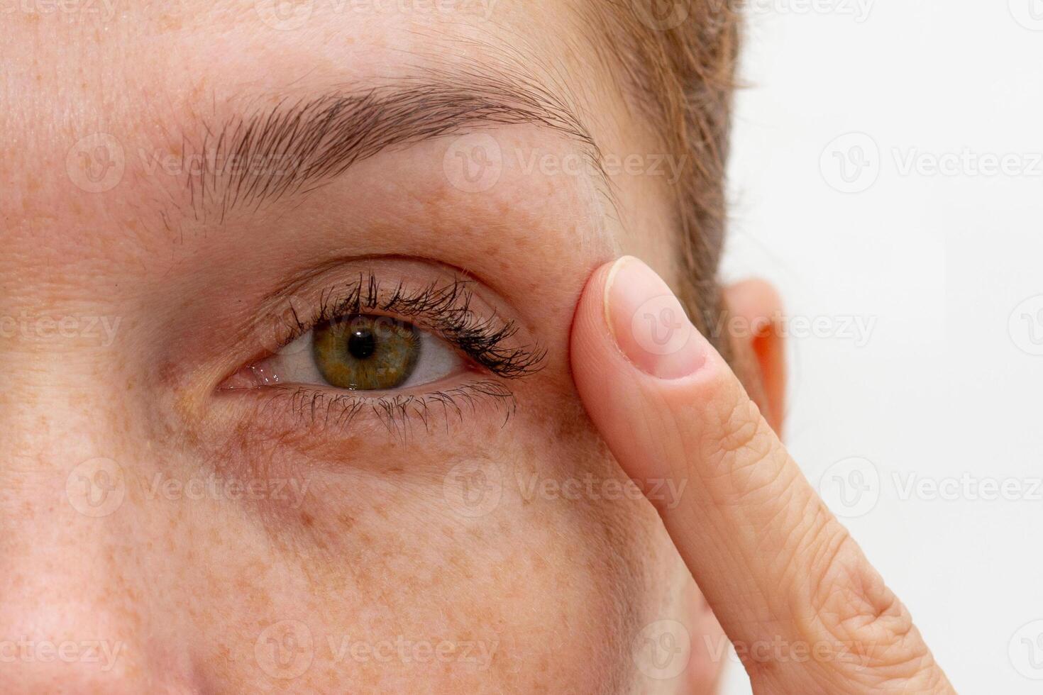 Close up cropped eye of middle aged caucasian woman looking at camera holding finger on eyelid photo