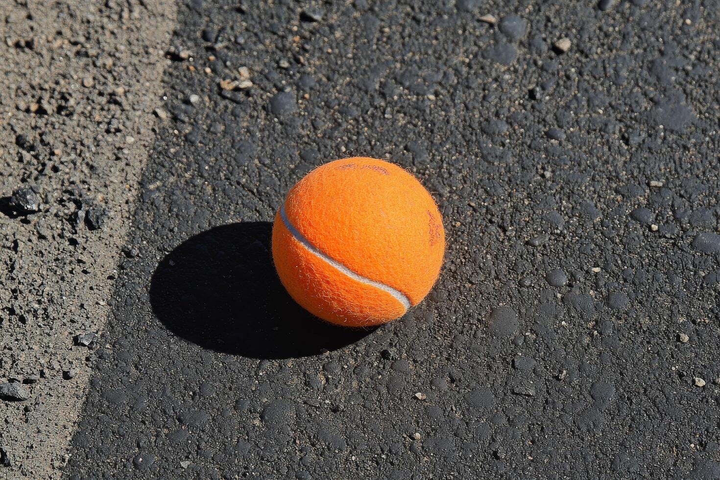 Bright orange tennis ball resting on a textured dark surface in a dramatic setting photo
