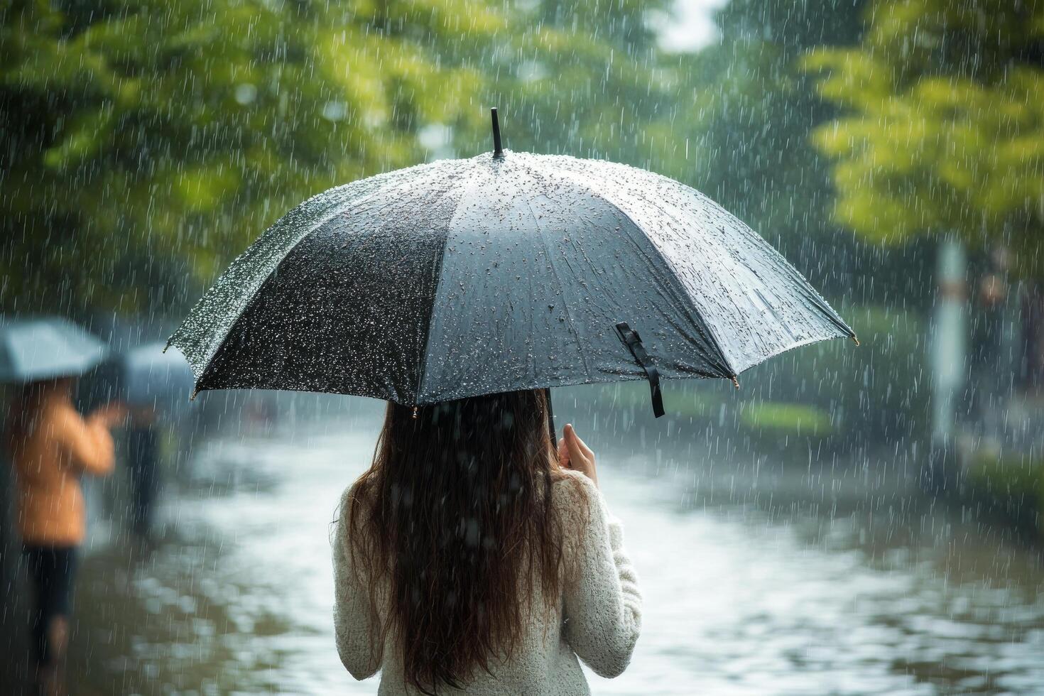 Woman enjoying autumn rain under a black umbrella in a park with vibrant yellow leaves photo
