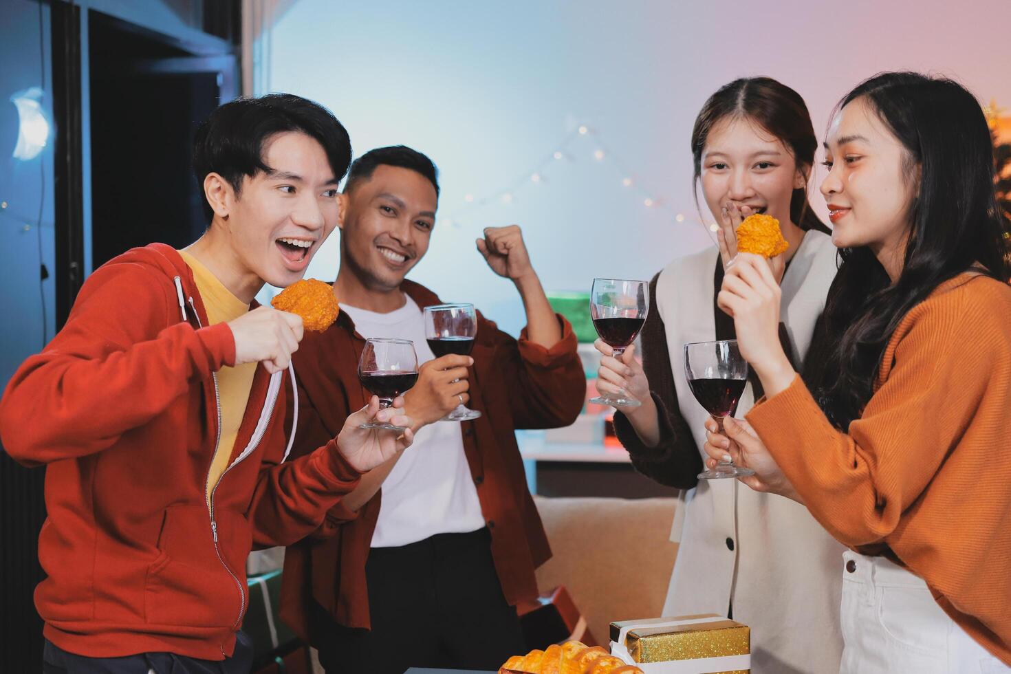 Group of young Asian man and women as friends having fun at a New Year's celebration, holding gift boxes standing by Christmas tree decoration, midnight countdown Party at home with holiday season. photo