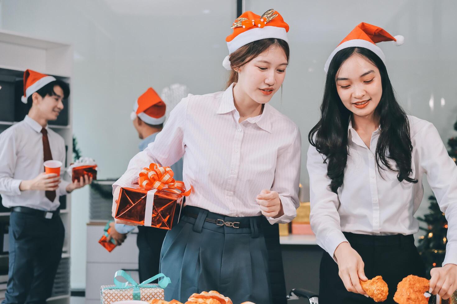 full length view of a group of business team wearing red Santa hat and exchange gift box together in the office for Christmas. photo