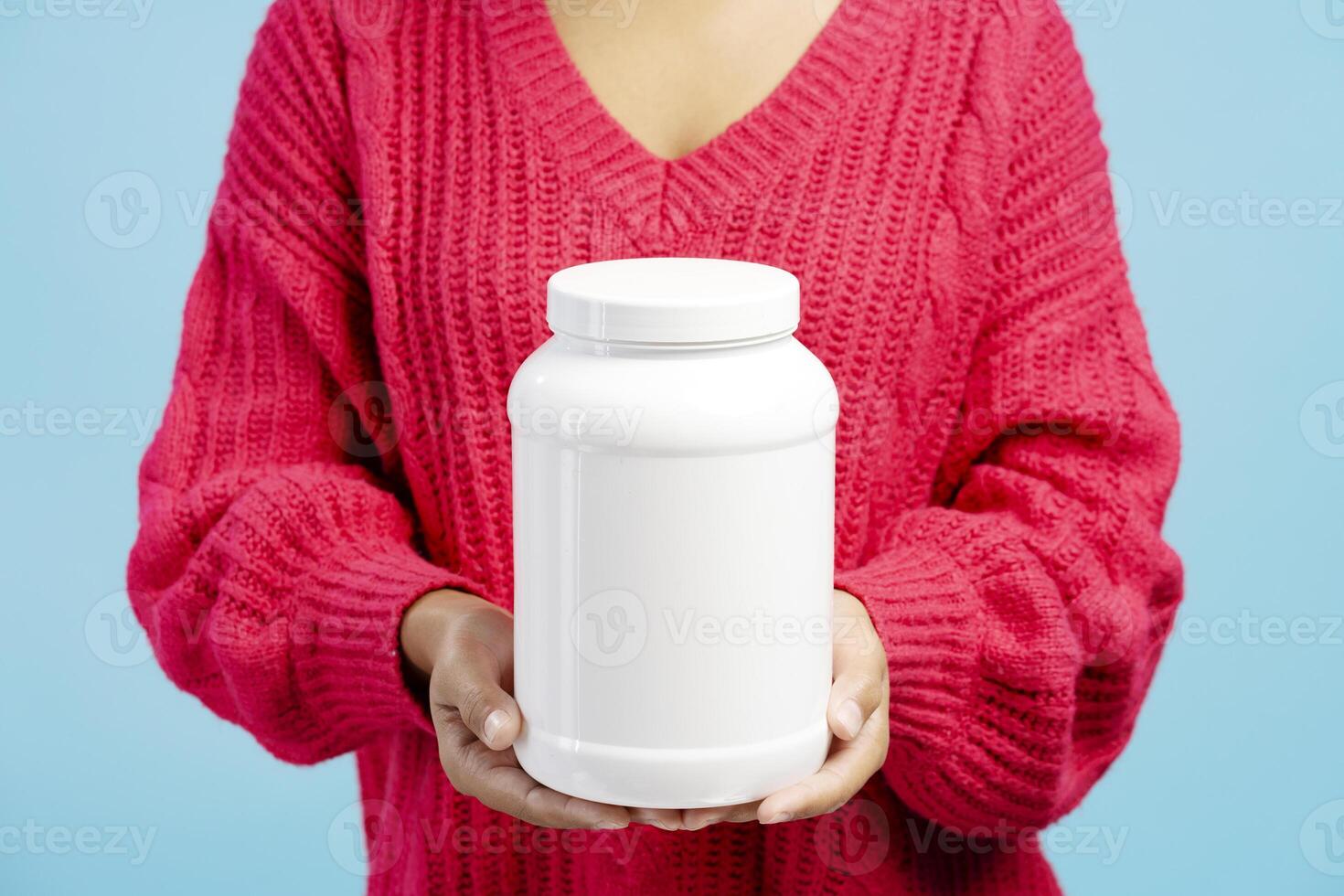 Woman holding a white plastic jar of protein powder on blue background photo