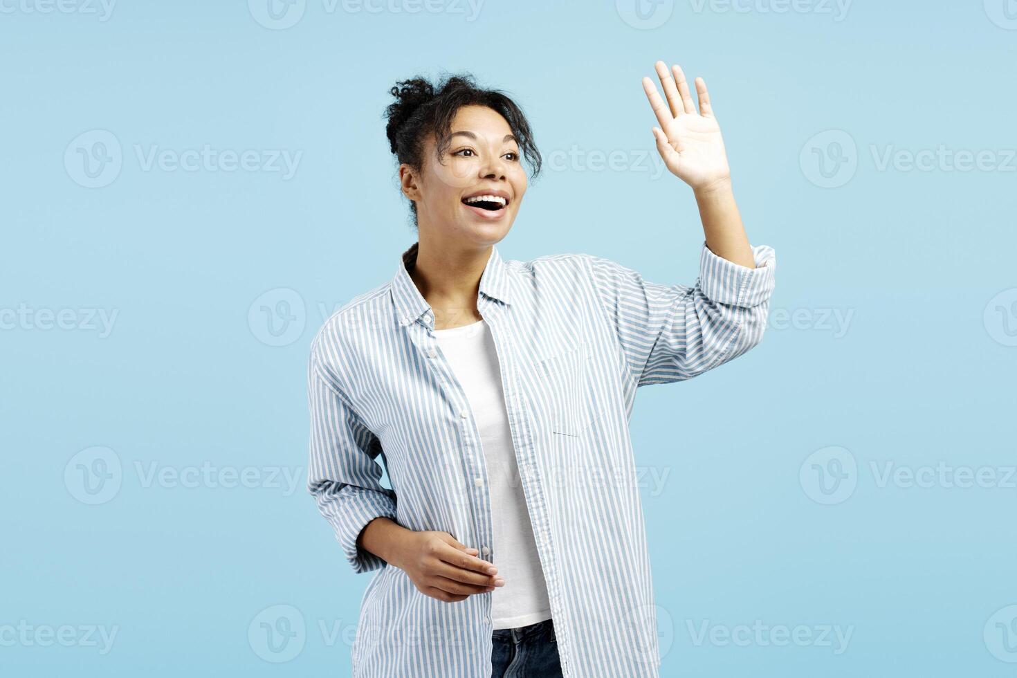 Cheerful young woman waving and smiling on blue background photo
