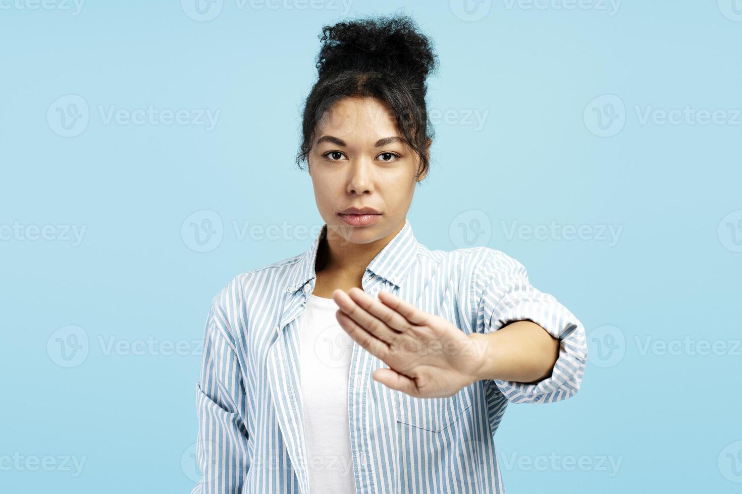 Serious young woman showing stop sign with hand on blue background photo