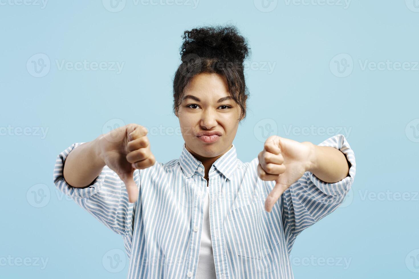 Young woman showing thumbs down gesture expressing dislike on blue background photo
