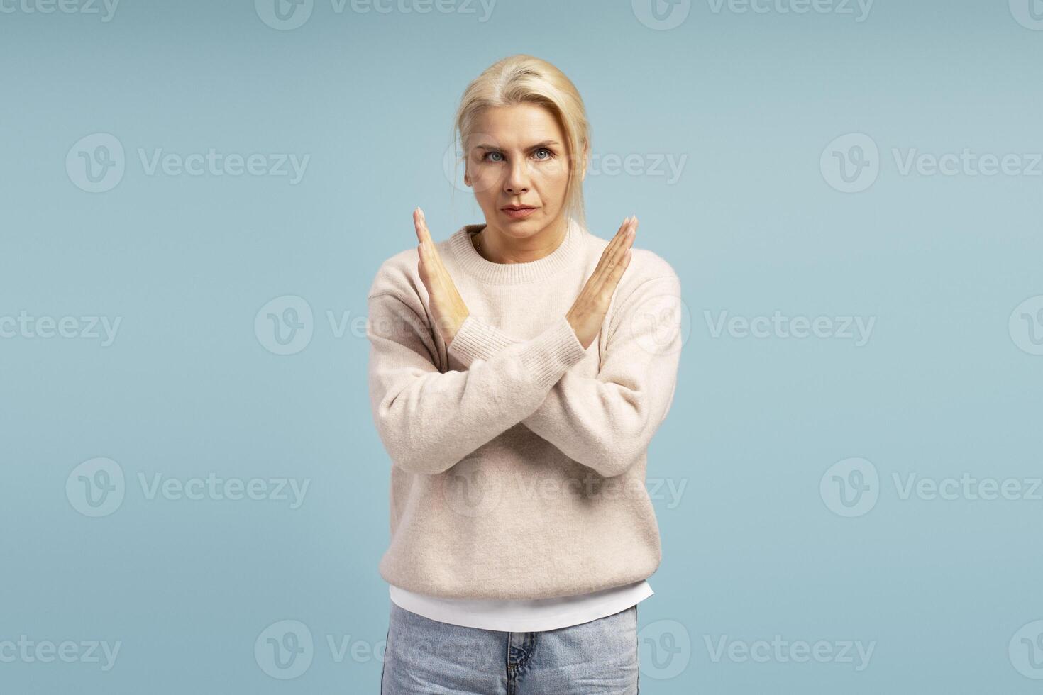 Serious woman showing stop sign with crossed arms on blue background photo