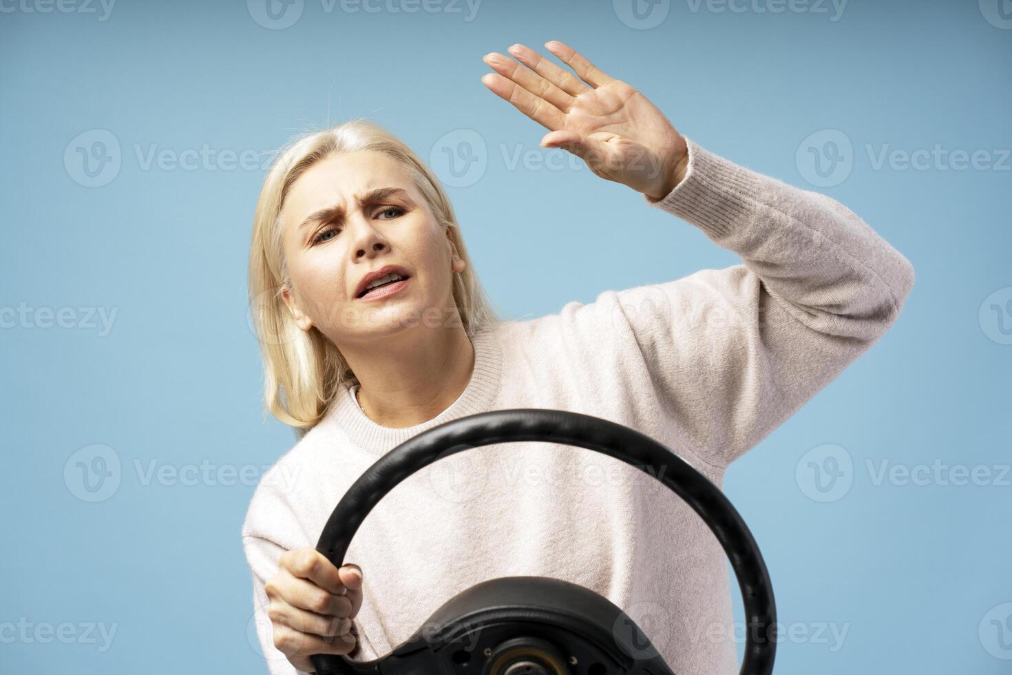 Scared mature woman protecting herself while driving with steering wheel on blue background photo