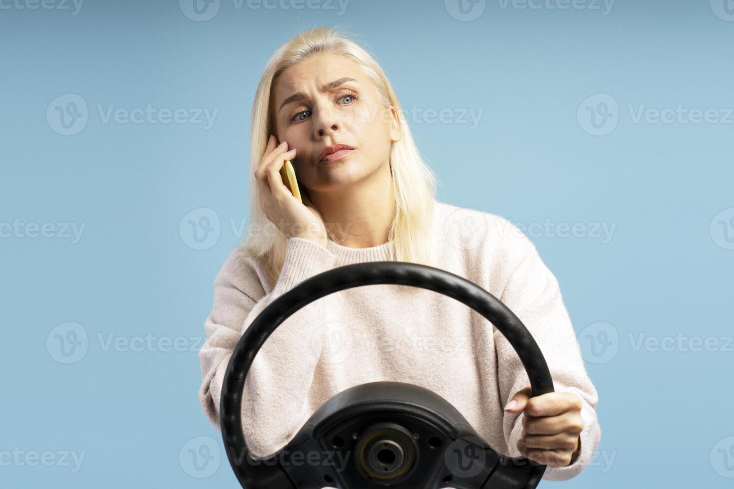 Blonde woman holding steering wheel and talking on phone with worried expression photo