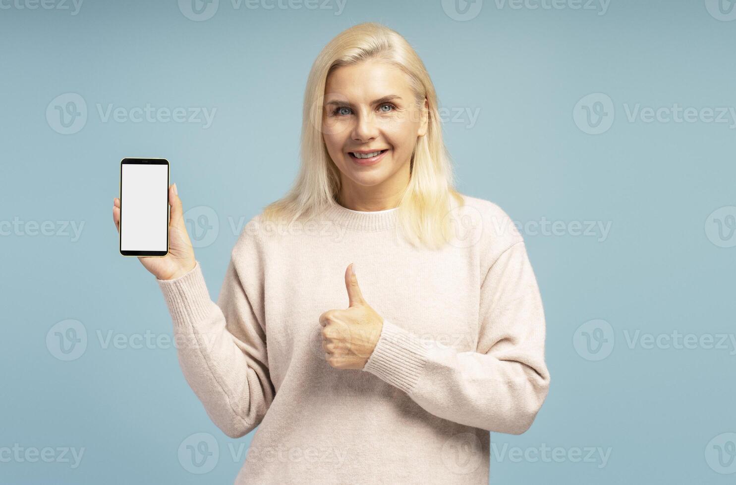Smiling woman showing smartphone with blank screen and giving thumb up photo