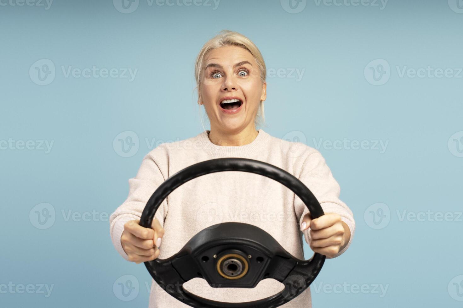 Excited woman holding steering wheel on blue background photo