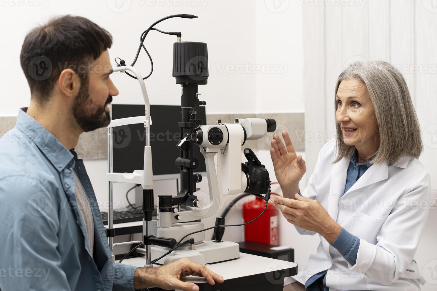 Senior female doctor performing eye exam on male patient using phoropter in ophthalmology clinic photo
