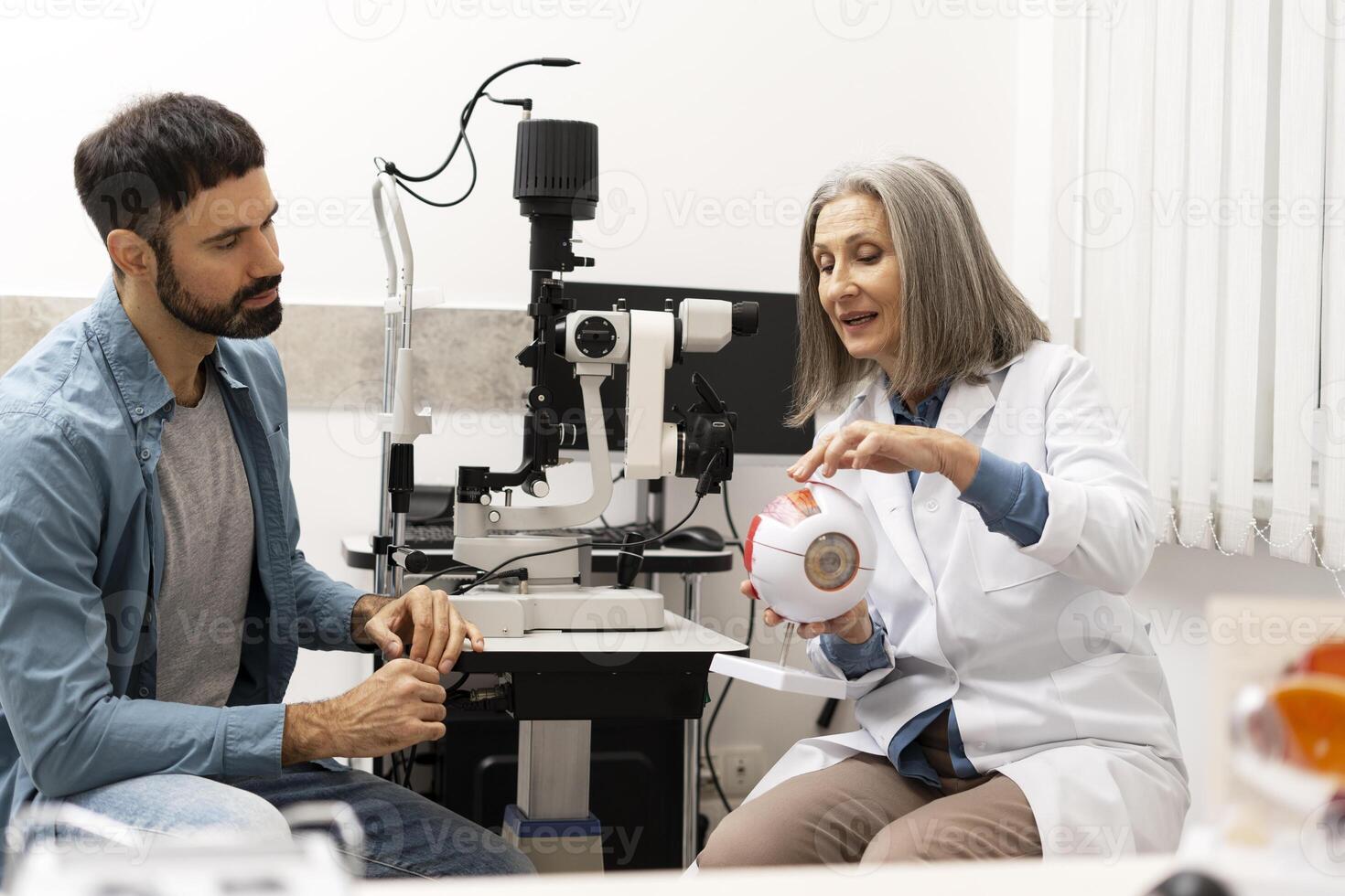 Senior female doctor explaining eye anatomy to patient using model in ophthalmology clinic photo