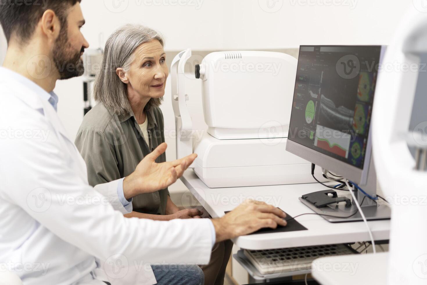 Ophthalmologist explaining diagnosis to senior patient using computer in clinic photo
